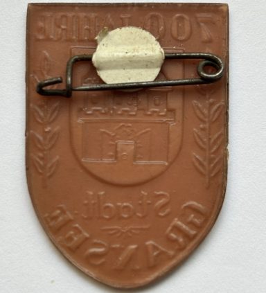 Emblem zum 700-jährigen Jubiläum der Stadt Gransee, mit einem Wappen und zwei stilisierten Ästen.
