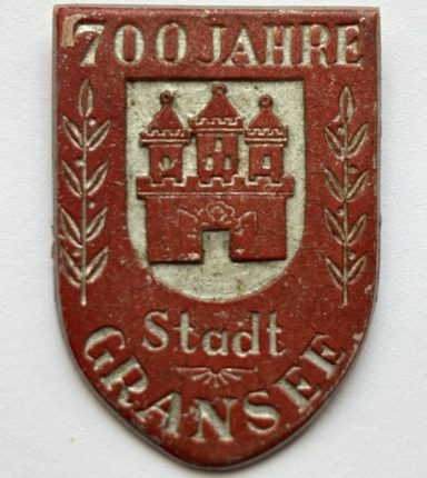 Emblem zum 700-jährigen Jubiläum der Stadt Gransee, mit einem Wappen und zwei stilisierten Ästen.