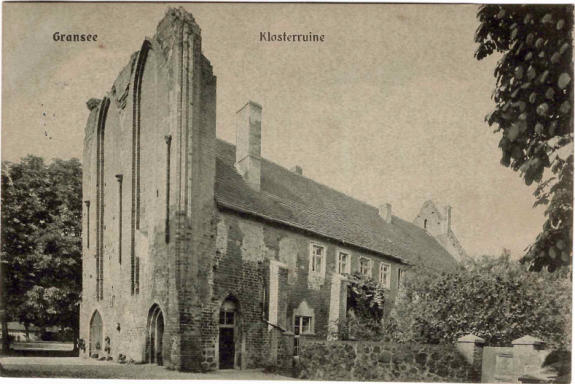 Historisches Gebäude mit offenen Fenstern und hohem Dach, umgeben von Bäumen.